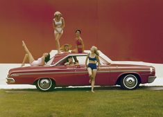 four women in bathing suits standing on top of a red car