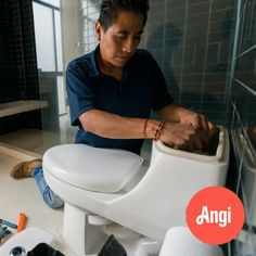 a man sitting on top of a white toilet in a bathroom next to other items