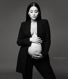 a pregnant woman poses for a black and white photo with her hands on her stomach