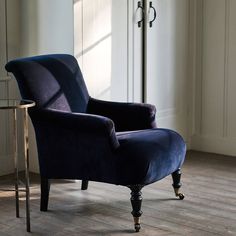 a blue velvet chair sitting in front of a glass table next to a window with white curtains