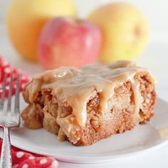 a piece of apple pie on a plate with a fork and two apples in the background