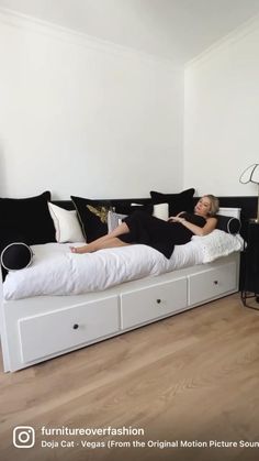 a woman laying on top of a bed in a room with white walls and wooden floors