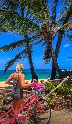 a woman standing next to a pink bike on the beach