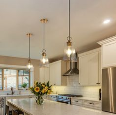 a kitchen with white cabinets and marble counter tops, two pendant lights over the island