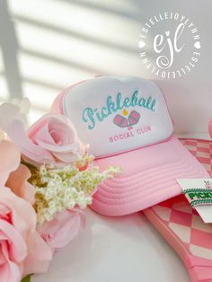 a pink trucker hat sitting on top of a table next to flowers and a pair of scissors