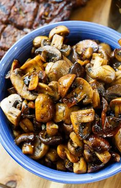 a blue bowl filled with mushrooms sitting on top of a wooden table next to meat