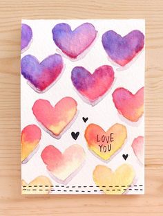 a card with watercolor hearts and the words love you written on it in different colors