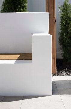 a white bench sitting on top of a stone floor next to a wooden door and shrubbery