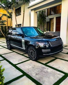 a black range rover parked in front of a house with palm trees on the side