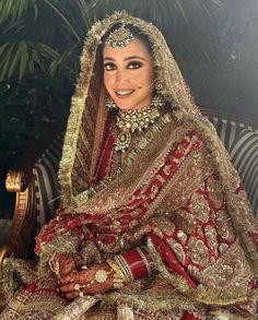 a woman in a red and gold bridal outfit sitting on a bench with her hands clasped