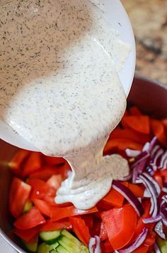 a bowl filled with vegetables and dressing being poured into it