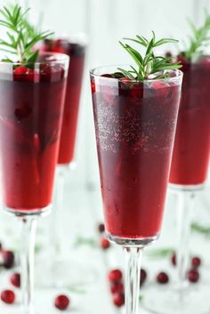 three glasses filled with red liquid and garnished with greenery