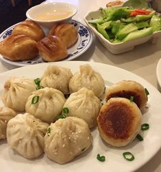 some dumplings are sitting on a white plate with green vegetables and dipping sauces