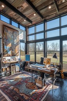 an artist's studio with large windows and lots of art work on the desk