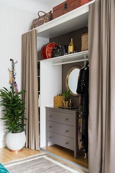 an open closet with clothes and other items on the shelves next to a plant in a vase