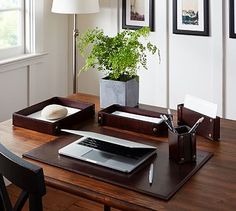 a wooden desk with a laptop computer on it and a potted plant in the corner