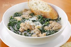 a white bowl filled with meat and spinach next to a piece of bread on top of a plate