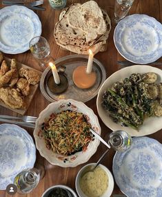 a wooden table topped with plates and bowls filled with food covered in sauces next to two lit candles