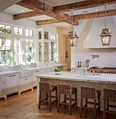 a large kitchen with white cabinets and wooden beams on the ceiling, along with wicker bar stools