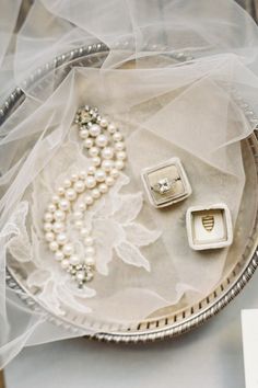 two wedding rings and pearls in a silver tray on a white cloth covered tablecloth