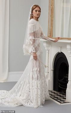 a woman standing in front of a fireplace wearing a wedding dress with long sleeves and a veil