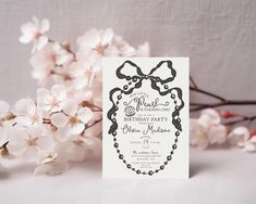 a white card with a black bow on it sitting next to some flowers and branches