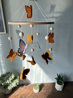 a mobile with butterflies hanging from it on a table next to a potted plant