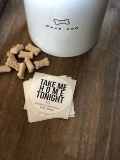 some dog treats are on the table next to a mug and sticker that says take me home tonight