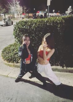 two young women sitting on the curb talking on their cell phones while one holds her hand up to her ear