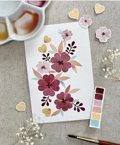 a card with flowers painted on it next to paintbrushes and watercolor paints