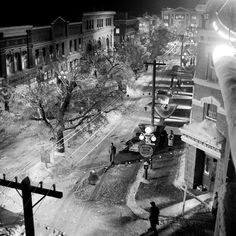 a black and white photo of an old town at night with people walking on the street