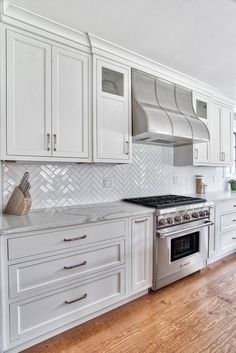 a kitchen with white cabinets and stainless steel stove top oven, range hood, and wood flooring