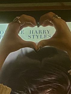 a person making a heart shape with their hands in front of a sign that says harry styles