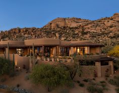 an adobe style house in the desert with mountains in the back ground and lights on