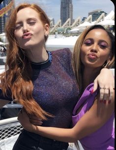 two beautiful young women standing next to each other on a boat in front of a city skyline