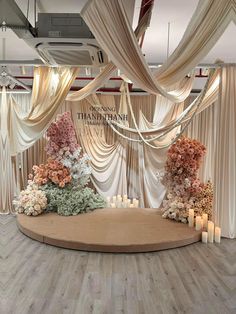 a round table with flowers and candles on it in front of a white drapes