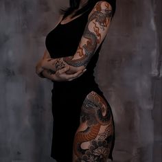 a woman with dragon tattoos on her arm and leg, standing in front of a wall