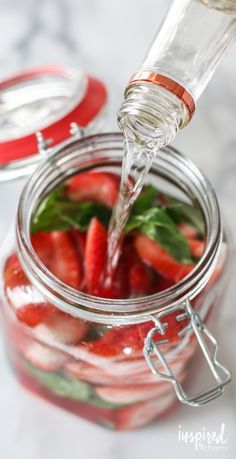 a glass jar filled with sliced strawberries and mint sprinkled with water being poured into it