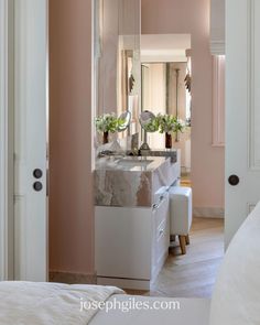 a bathroom with pink walls and marble counter tops, along with a white bed in the foreground