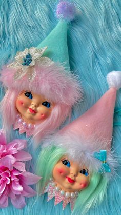 two pink and green gnomes with flowers on a blue fur surface next to each other