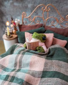 a stuffed frog sitting on top of a bed next to a candle and some pillows