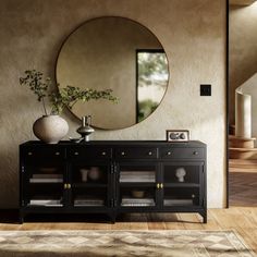 a large round mirror hangs on the wall above a black cabinet with glass doors and drawers