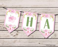 pink and green floral banner with the letters ah on it hanging from a line against a wooden background