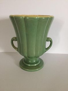 a green vase sitting on top of a white table next to a wall and floor