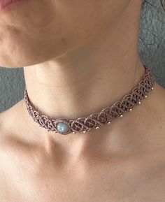 a woman wearing a pink choker with beads on the bottom and a blue stone in the middle