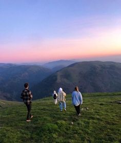 four people standing on top of a grass covered hill with mountains in the back ground