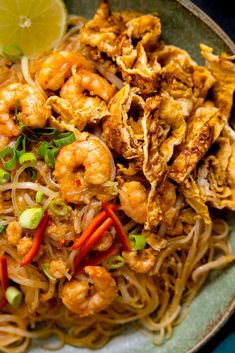 a plate filled with noodles and shrimp next to a lemon wedge