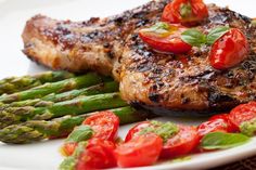 grilled steak with asparagus and tomatoes on a white plate, ready to be eaten