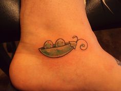 a small foot tattoo with two peas in a boat on it's back side