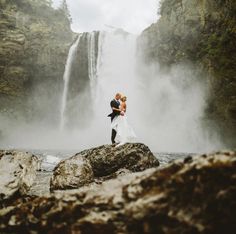 a bride and groom standing in front of a waterfall